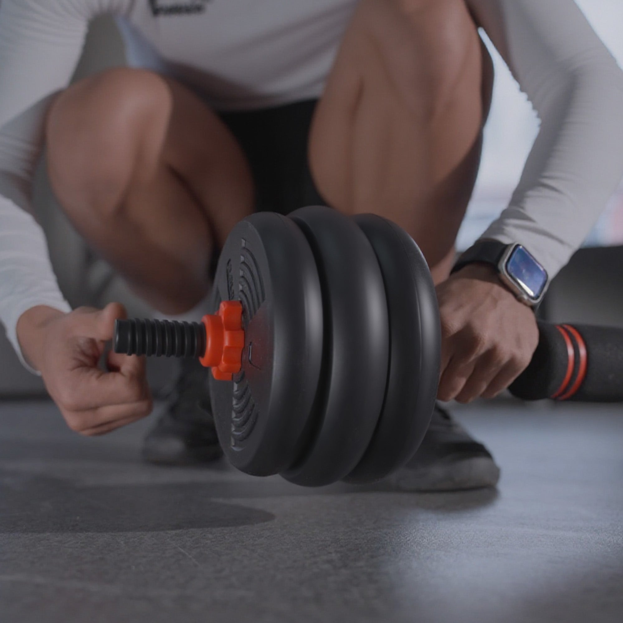 Person adjusting a dumbbell on a gray floor