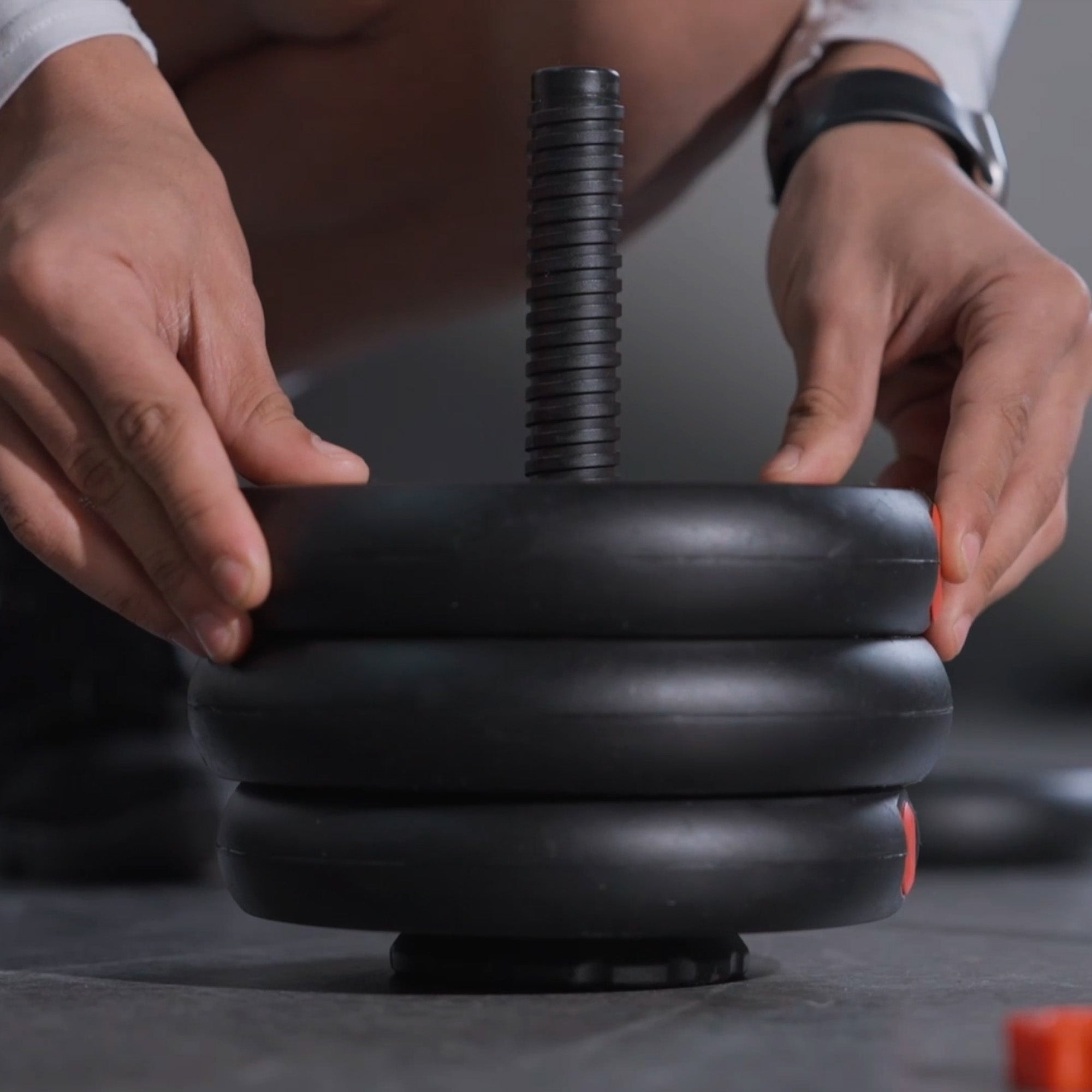 Person assembling a black adjustable dumbbell on a dark surface.