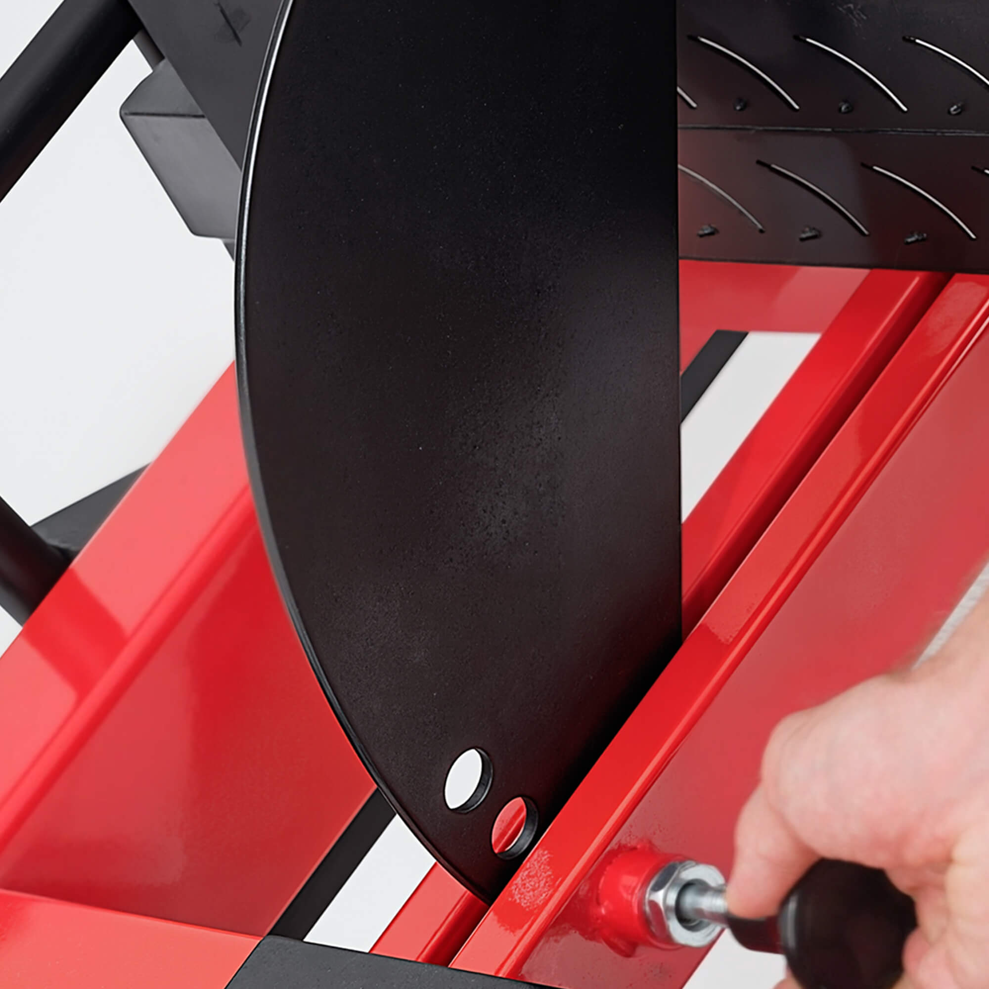 Person using a tool to adjust a black metal component on a red machine.#color_red