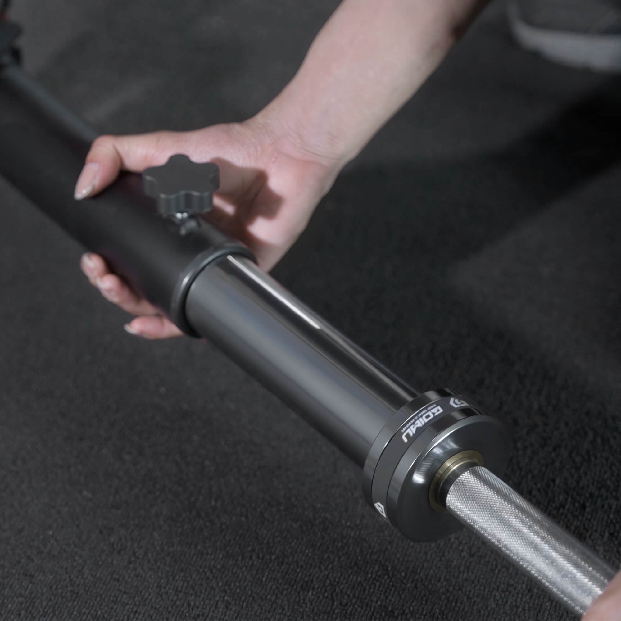 Person adjusting a black and silver adjustable stand on a dark background.
