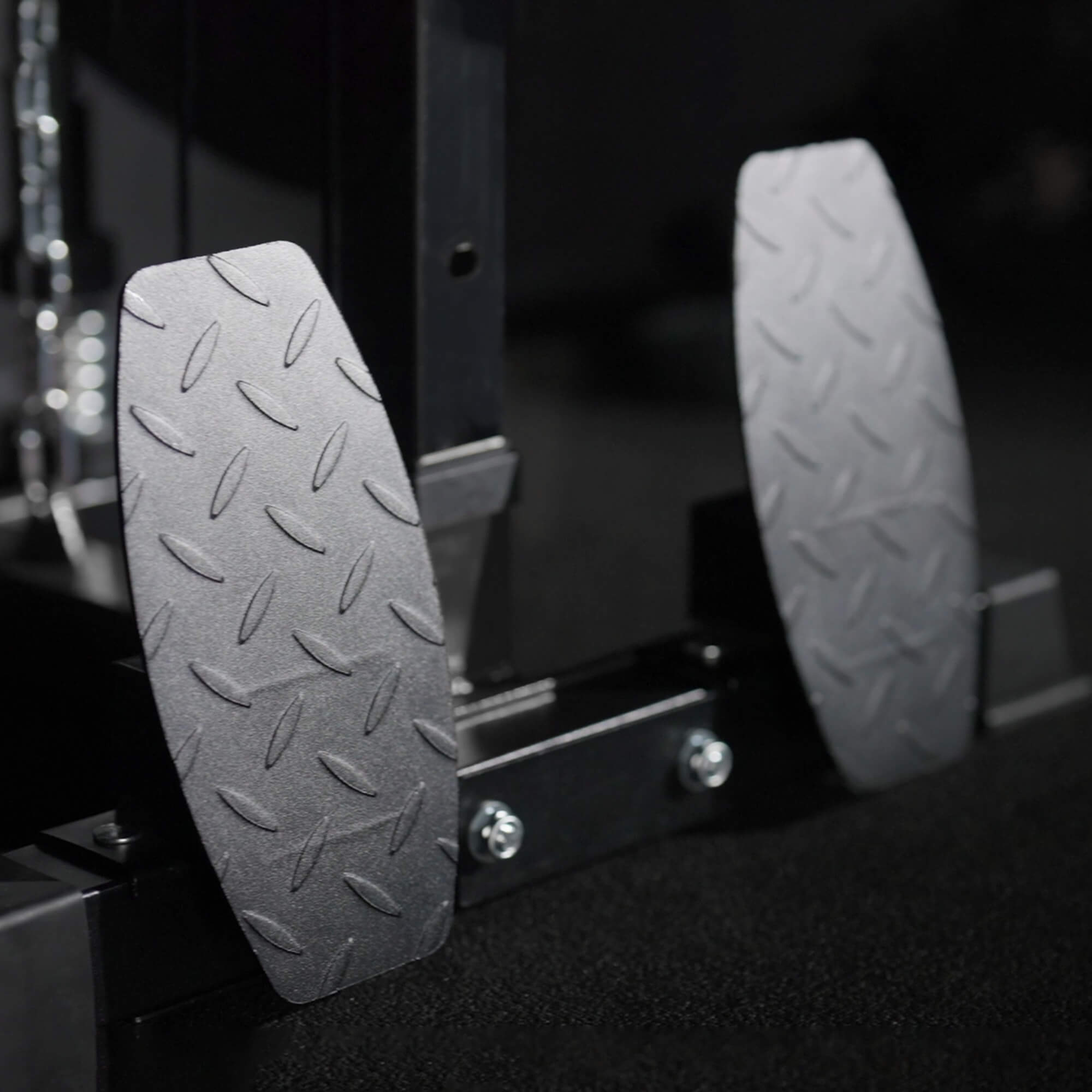 Close-up of two metallic foot pedals with textured surfaces on a dark background.