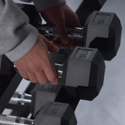 Person holding a pair of hexagonal dumbbells with weight markings.#pounds_550lbs-with-rack