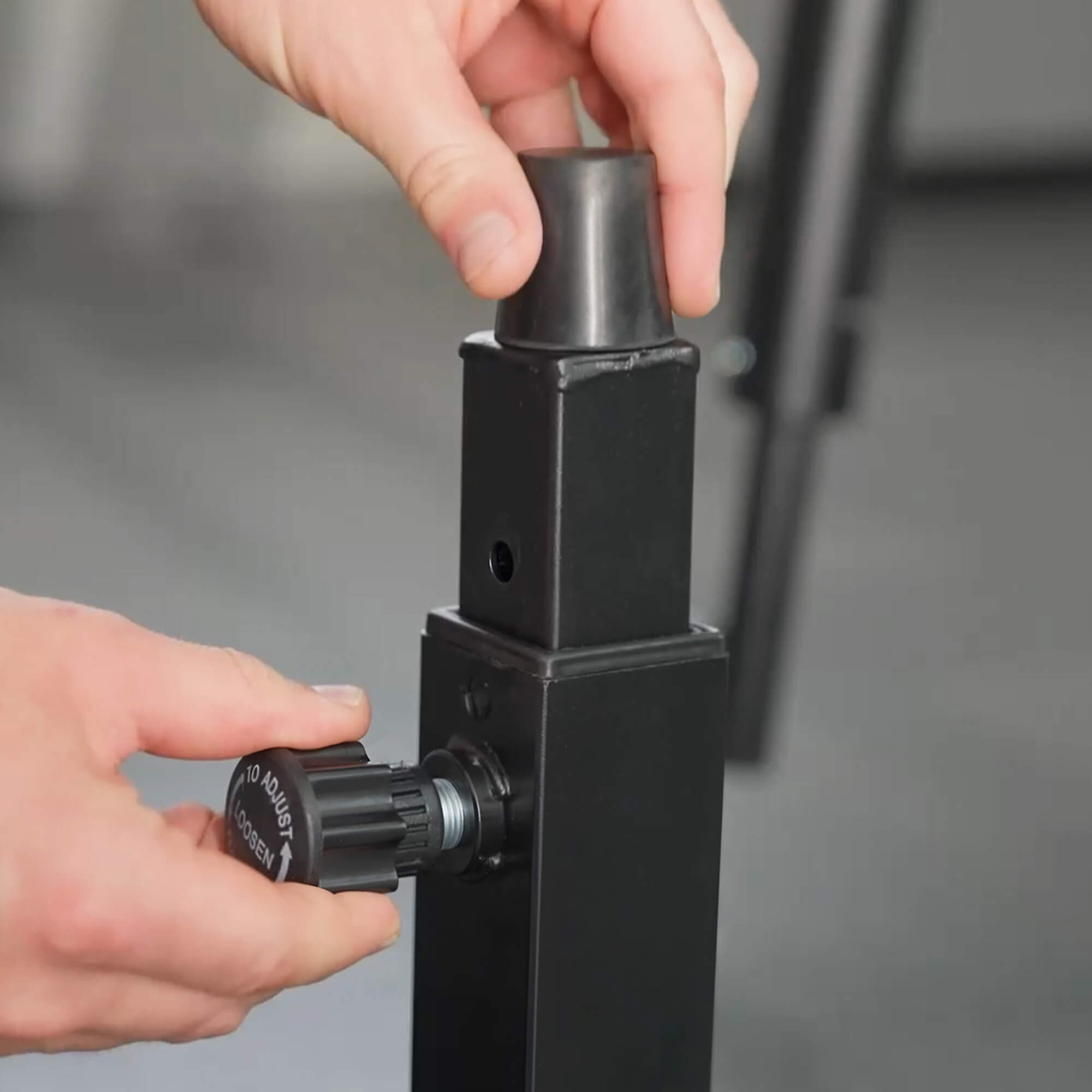 Person adjusting a black metal component with a screwdriver on a gray background.