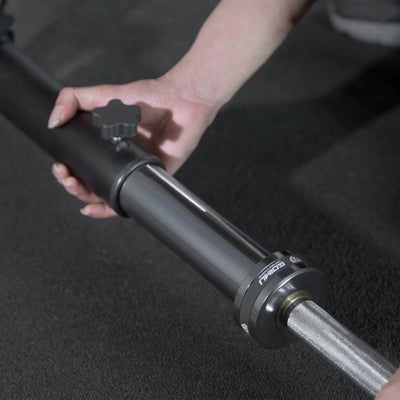 Person adjusting a black and silver adjustable stand on a dark background.