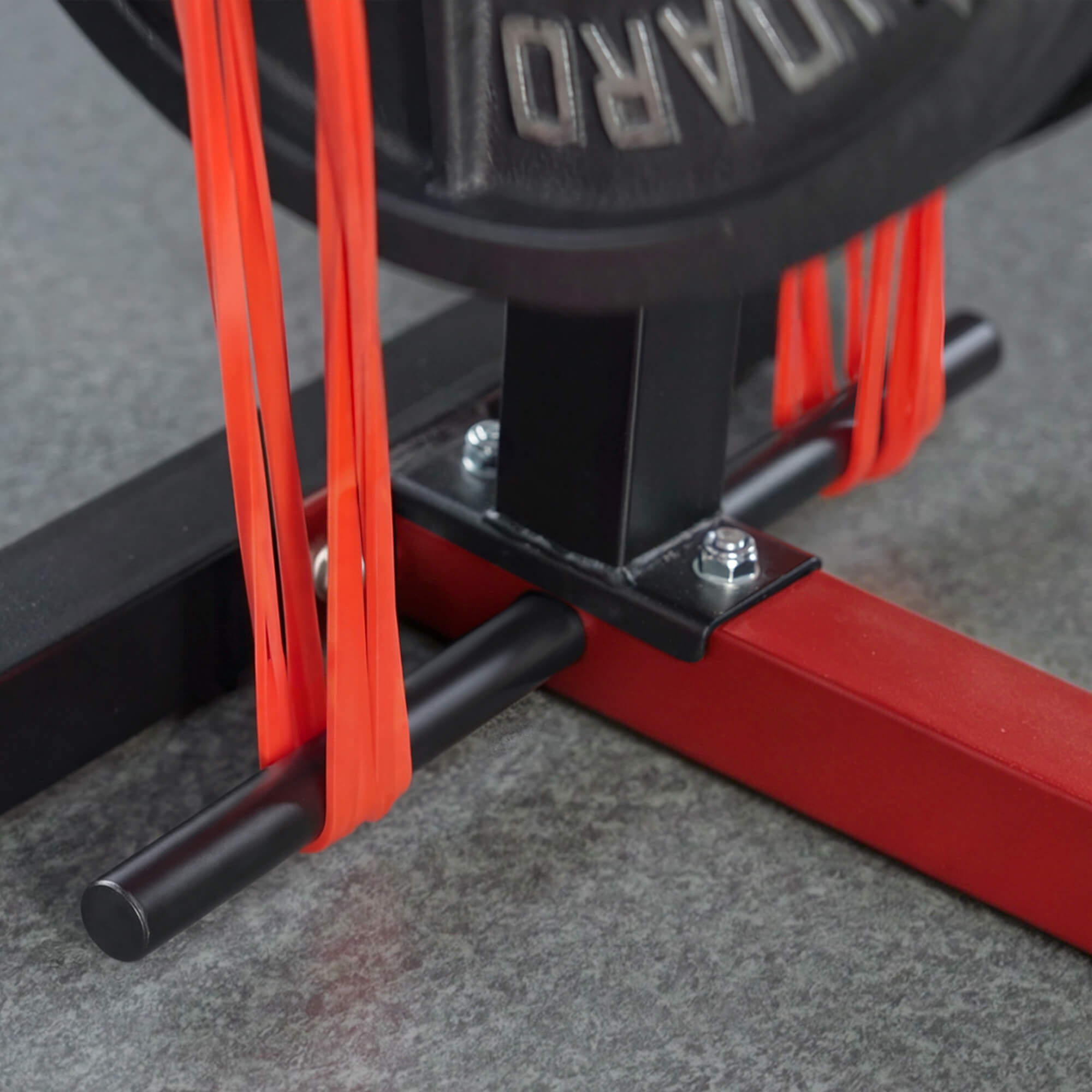 Close-up of a red resistance band attached to a black barbell on a gray floor.