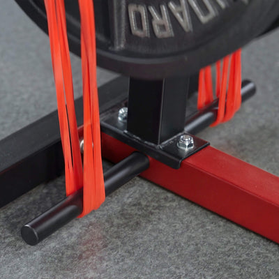 Close-up of a red resistance band attached to a black barbell on a gray floor.