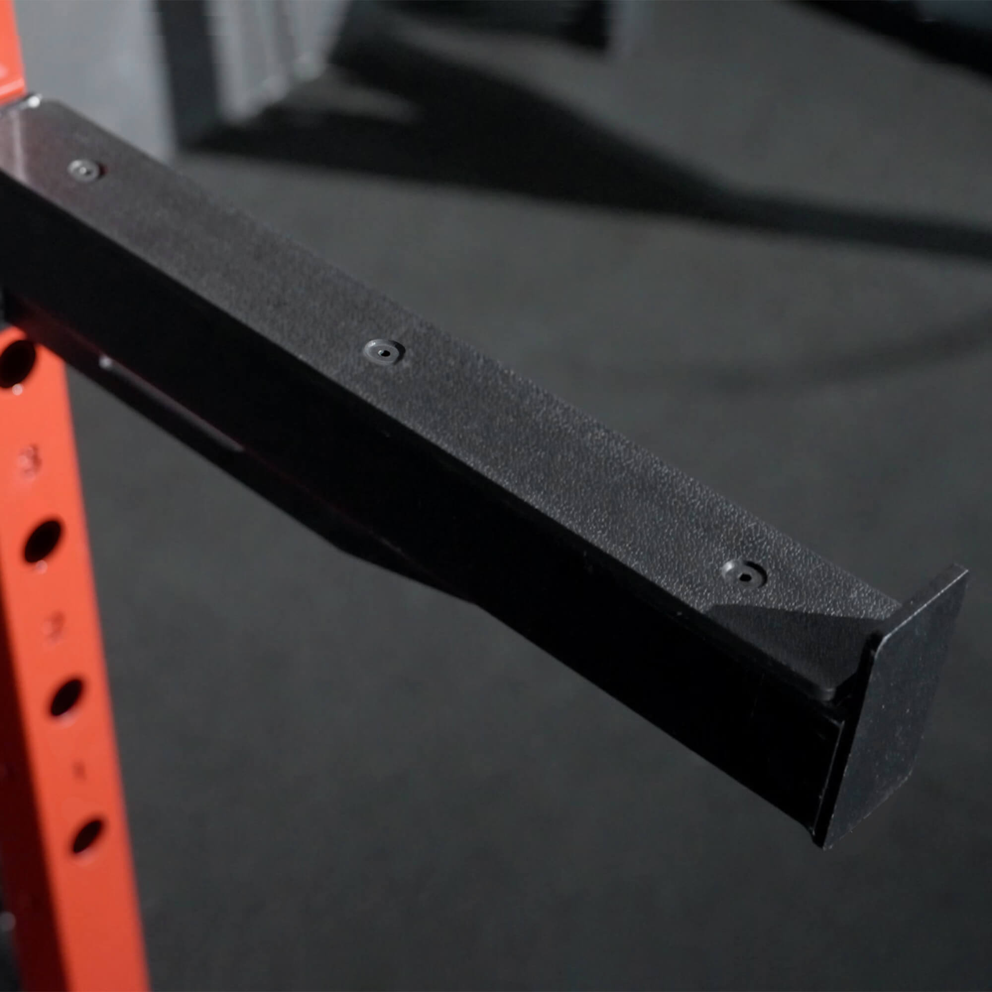 Black metal bracket attached to a red and black exercise rack on a dark background.
