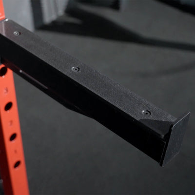 Black metal bracket attached to a red and black exercise rack on a dark background.