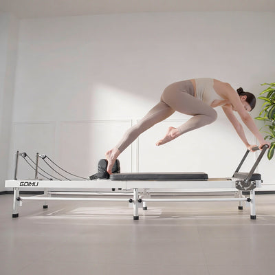 Woman exercising on a Pilates reformer machine in a studio setting.