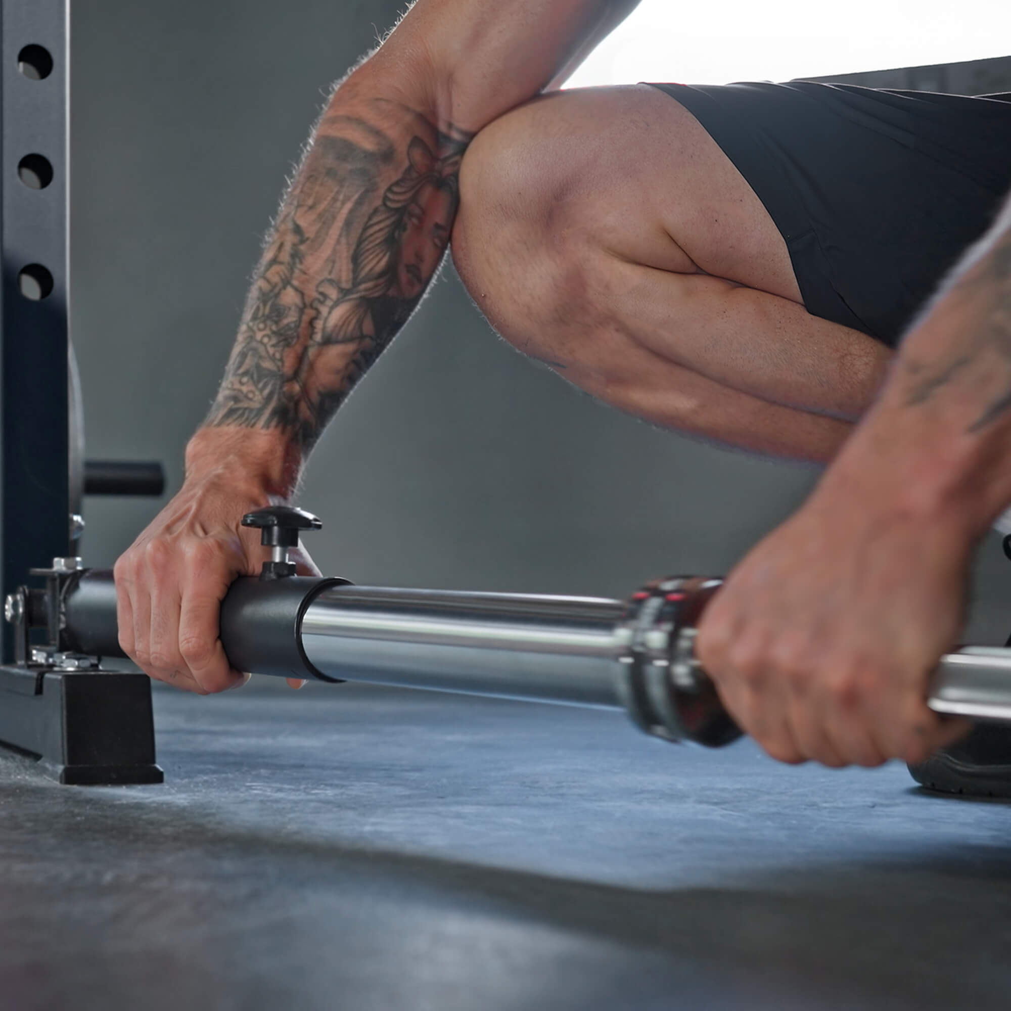 Person adjusting gym equipment with tattoos on arms.