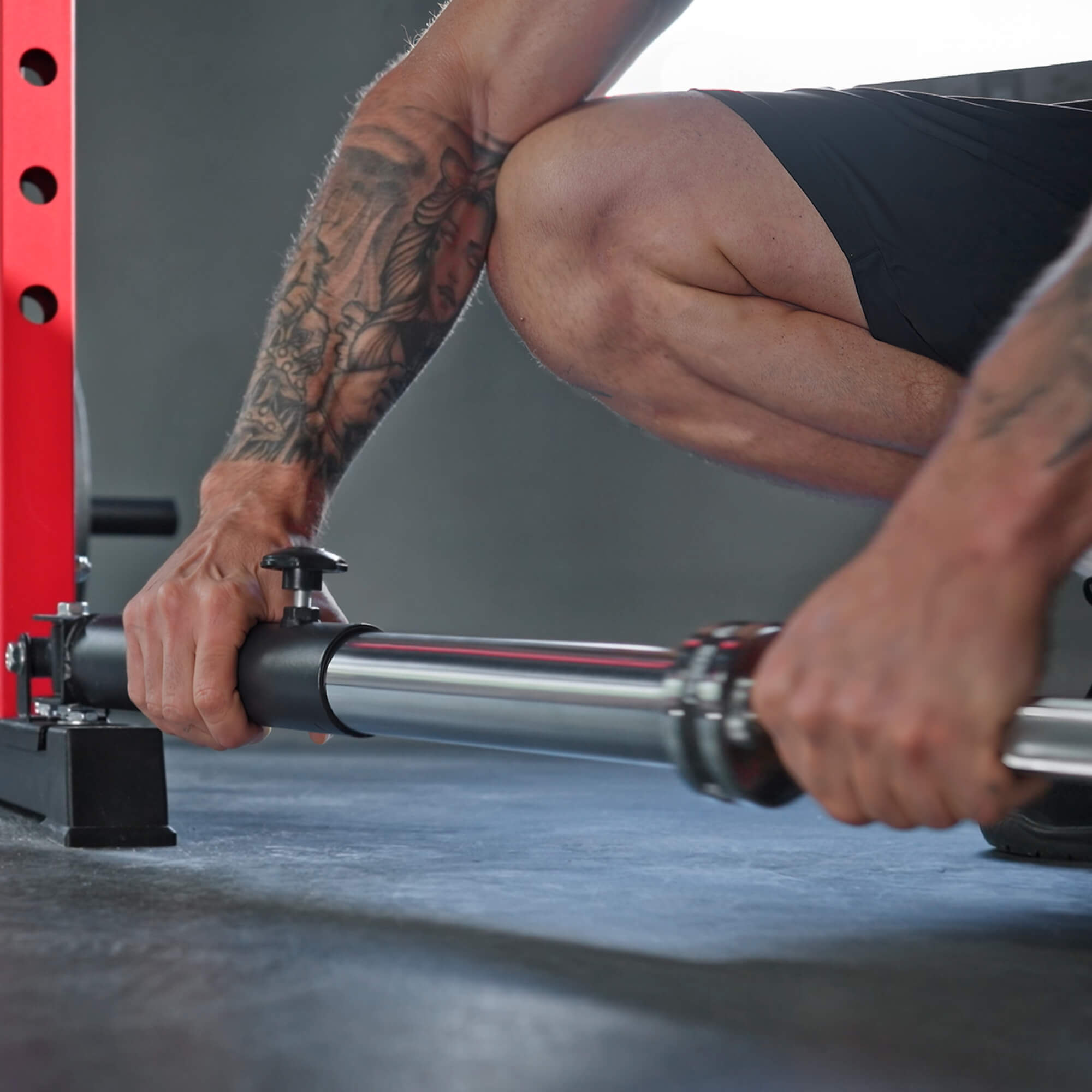 Person adjusting gym equipment with tattoos on arms.