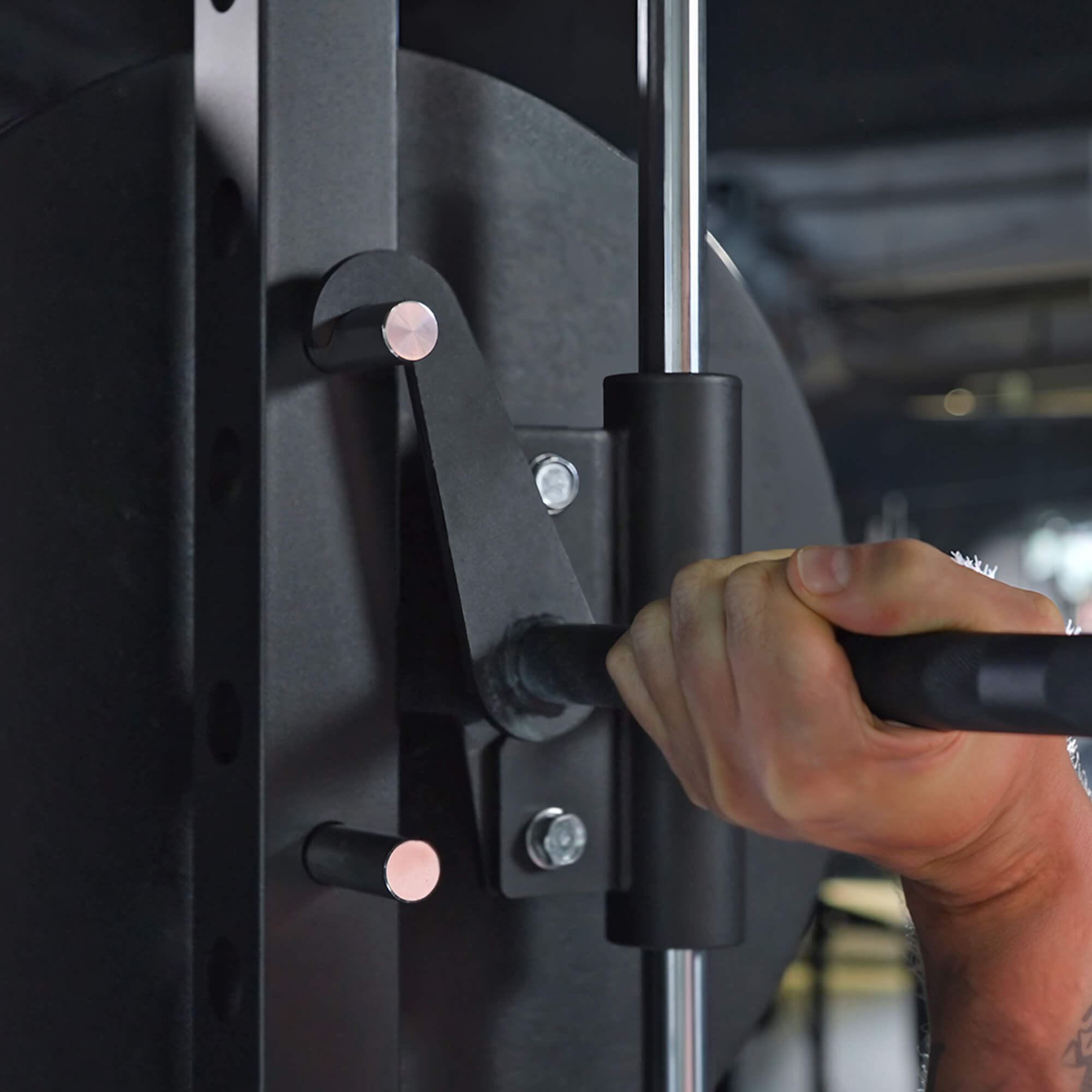 Hand adjusting a black gym machine with blurred background.