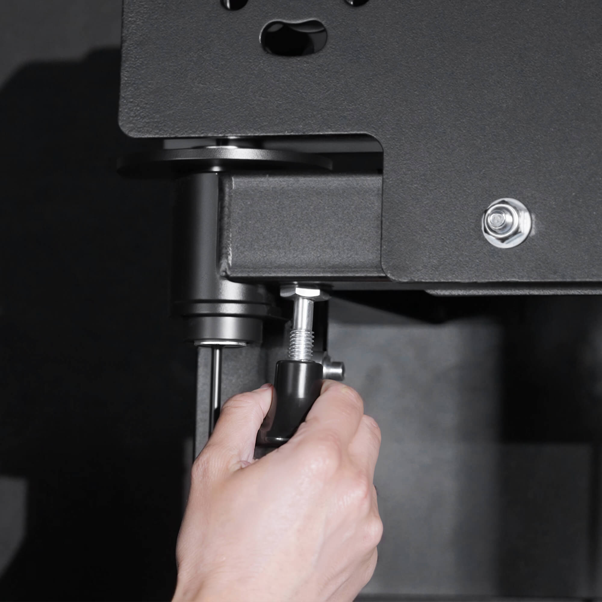 Hand adjusting a screw on a piece of equipment with a dark background.